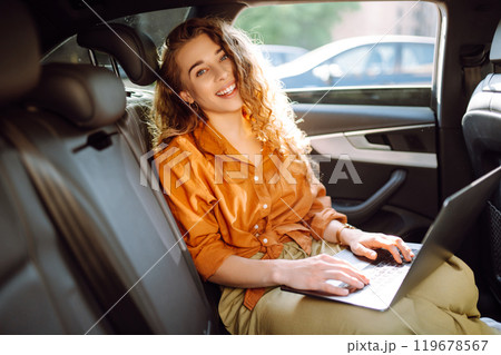 Beautiful business woman is using a laptop while sitting in the back seat of car. Freelance concept. Beautiful business woman is using a laptop while sitting in the back seat of car. Freelance concept. 119678567