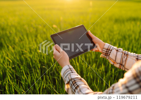 Experienced woman farmer with digital tablet in hands on green wheat field. Concept of gardening. Experienced woman farmer with digital tablet in hands on green wheat field. Concept of gardening. 119679211