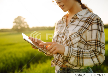 Experienced woman farmer with digital tablet in hands on green wheat field. Concept of gardening. Experienced woman farmer with digital tablet in hands on green wheat field. Concept of gardening. 119679213