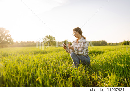 Experienced woman farmer with digital tablet in hands on green wheat field. Concept of gardening. 119679214