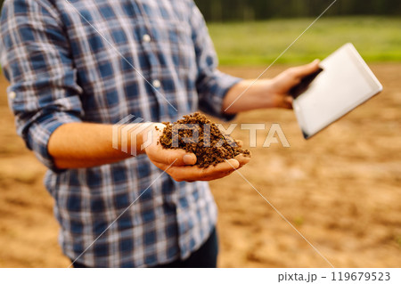 Farmer in a sunny field collects soil, checks its health using a digital tablet. Technology concept 119679523