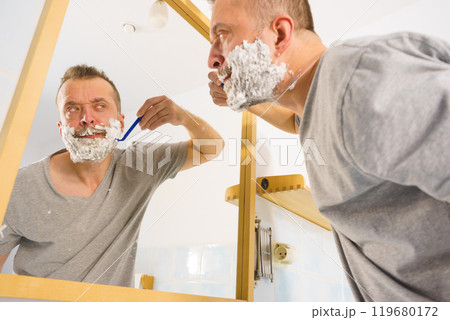 Guy shaving his beard in bathroom Guy shaving his beard in bathroom 119680172
