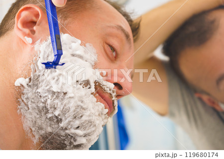 Guy shaving his beard in bathroom Guy shaving his beard in bathroom 119680174