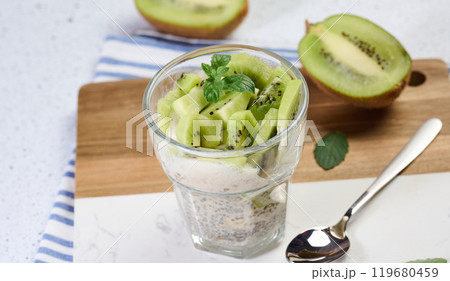 Glass with chia and yogurt dessert garnished with fresh kiwi slices on white table 119680459