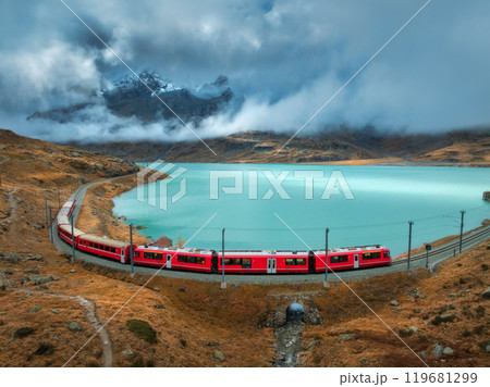 Aerial view of red train near alpine mountain lake and cloudy sky 119681299
