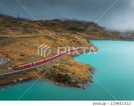 Aerial view of red train near alpine mountain lake and cloudy sky 119681312