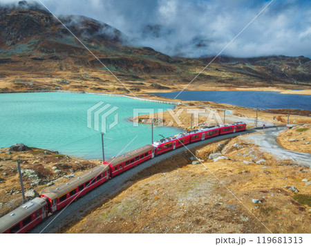 Aerial view of red train near alpine mountain lake and cloudy sky 119681313