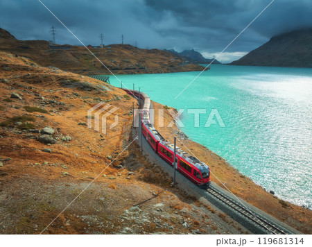 Aerial view of red train near alpine mountain lake and cloudy sky 119681314