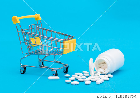 Scattered Pills or Capsules and Shopping Cart on Blue Background Scattered Pills or Capsules and Shopping Cart on Blue Background 119681754