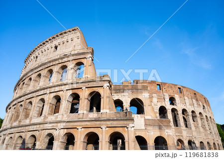 Visitors admire the majestic Colosseum in Rome, Italy, marveling at its ancient architecture against a clear blue sky, showcasing the grandeur of this historic landmark. 119681838