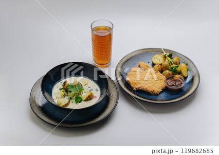 Complete lunch set with schnitzel, roasted potatoes, cold soup, and refreshing drink  119682685