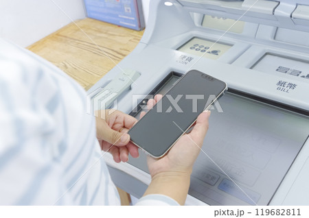 スマホを見ながらATMを操作する女性 119682811