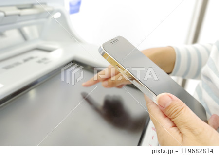 スマホを見ながらATMを操作する女性 スマホを見ながらATMを操作する女性 119682814