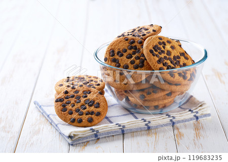 Delicious cookies with chocolate chips in a clear glass bowl with on a light kitchen table, selective focus. Delicious cookies with chocolate chips in a clear glass bowl with on a light kitchen table, selective focus. 119683235