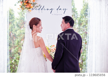 Small wedding - the priest is present, the bride and groom hold their wedding bouquets, hold hands, and share a beautiful moment with family and friends. 119685856