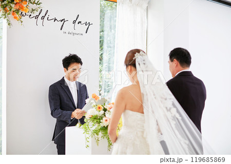 Small wedding - the priest is present, the bride and groom hold their wedding bouquets, hold hands, and share a beautiful moment with family and friends. 119685869