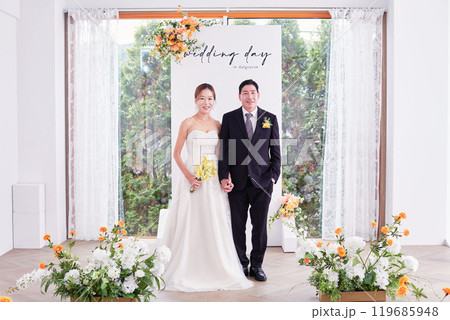 Small wedding - the priest is present, the bride and groom hold their wedding bouquets, hold hands, and share a beautiful moment with family and friends. 119685948
