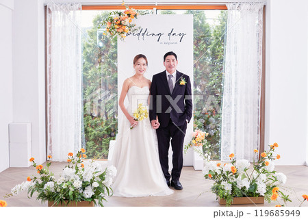 Small wedding - the priest is present, the bride and groom hold their wedding bouquets, hold hands, and share a beautiful moment with family and friends. 119685949