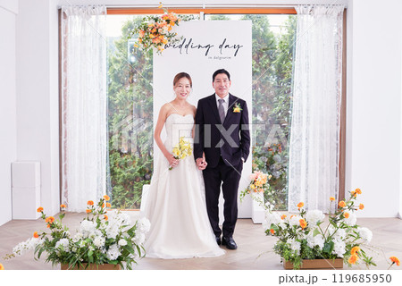 Small wedding - the priest is present, the bride and groom hold their wedding bouquets, hold hands, and share a beautiful moment with family and friends. 119685950