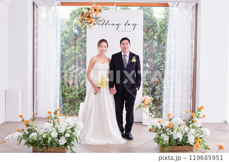 Small wedding - the priest is present, the bride and groom hold their wedding bouquets, hold hands, and share a beautiful moment with family and friends. 119685951