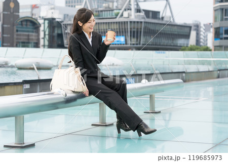 都会の真ん中でテイクアウトコーヒーを飲んでくつろぐ若いビジネスウーマン 都会の真ん中でテイクアウトコーヒーを飲んでくつろぐ若いビジネスウーマン 119685973