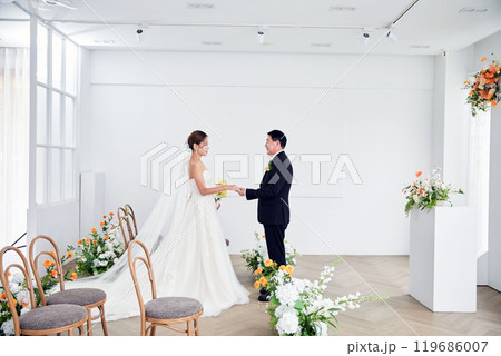 Small wedding - the priest is present, the bride and groom hold their wedding bouquets, hold hands, and share a beautiful moment with family and friends. 119686007