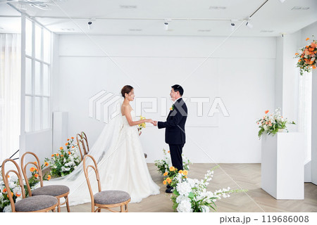 Small wedding - the priest is present, the bride and groom hold their wedding bouquets, hold hands, and share a beautiful moment with family and friends. 119686008