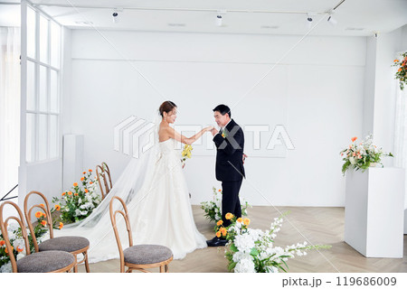 Small wedding - the priest is present, the bride and groom hold their wedding bouquets, hold hands, and share a beautiful moment with family and friends. 119686009