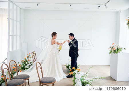 Small wedding - the priest is present, the bride and groom hold their wedding bouquets, hold hands, and share a beautiful moment with family and friends. 119686010