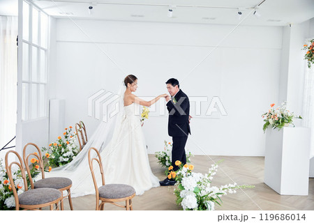 Small wedding - the priest is present, the bride and groom hold their wedding bouquets, hold hands, and share a beautiful moment with family and friends. Small wedding - the priest is present, the bride and groom hold their wedding bouquets, hold hands, and share a beautiful moment with family and friends. 119686014