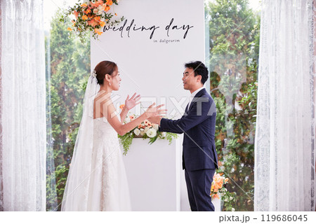 Small wedding - the priest is present, the bride and groom hold their wedding bouquets, hold hands, and share a beautiful moment with family and friends. 119686045