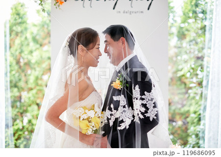 Small wedding - the priest is present, the bride and groom hold their wedding bouquets, hold hands, and share a beautiful moment with family and friends. 119686095