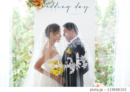 Small wedding - the priest is present, the bride and groom hold their wedding bouquets, hold hands, and share a beautiful moment with family and friends. 119686101