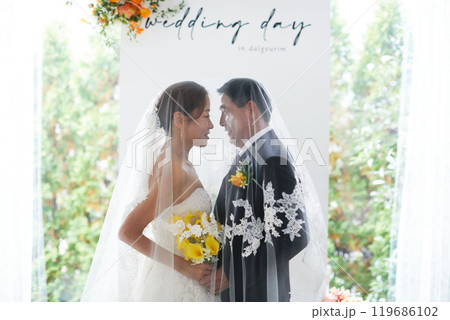 Small wedding - the priest is present, the bride and groom hold their wedding bouquets, hold hands, and share a beautiful moment with family and friends. 119686102