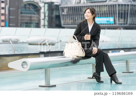 都会の真ん中でテイクアウトコーヒーを飲んでくつろぐ若いビジネスウーマン 119686169