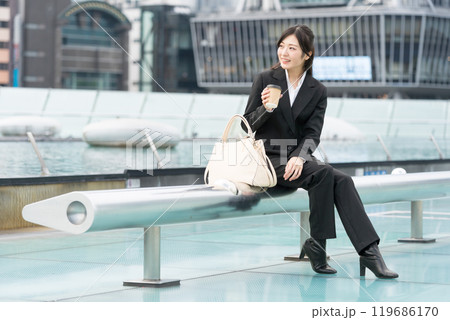 都会の真ん中でテイクアウトコーヒーを飲んでくつろぐ若いビジネスウーマン 119686170