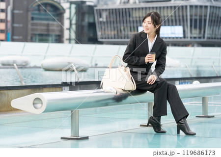 都会の真ん中でテイクアウトコーヒーを飲んでくつろぐ若いビジネスウーマン 119686173