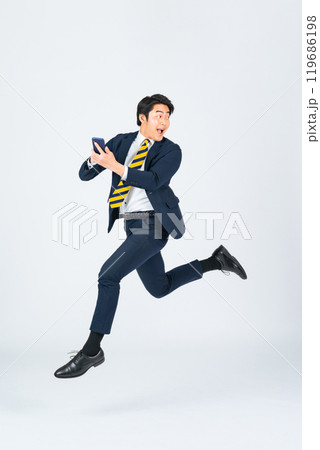 スマホを使いながらジャンプする若い男性ビジネスパーソンの全身写真 119686198