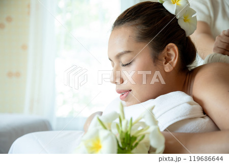 Young woman with eyes closed, receiving soothing herbal compress massage at spa, lying on towel surrounded with copy space 119686644