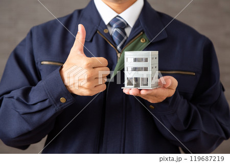 ビルの建築模型を持って親指を立てる作業着姿のミドル男性ビジネスマン 119687219