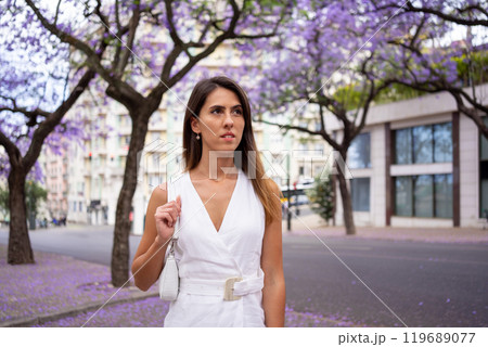 Thoughtful woman in white dress carrying purse in 119689077