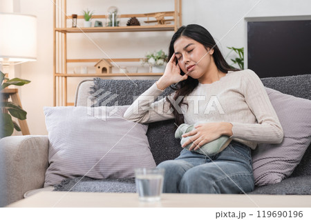 Young Woman Experiencing Abdominal Pain and Headache During Menstruation While Sitting on a Sofa at Home 119690196