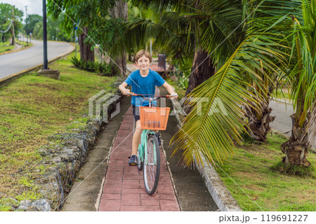 Boy tourist cycling through the charming village of Bacalar, Mexico. Quintana Roo travel, scenic bike paths, and eco-friendly exploration concept Boy tourist cycling through the charming village of Bacalar, Mexico. Quintana Roo travel, scenic bike paths, and eco-friendly exploration concept 119691227