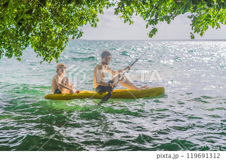 Father and son tourists kayaking on Bacalar Lake in Mexico. Adventure tourism in Quintana Roo, outdoor exploration, and water activities concept Father and son tourists kayaking on Bacalar Lake in Mexico. Adventure tourism in Quintana Roo, outdoor exploration, and water activities concept 119691312