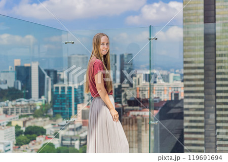 Female tourist or businesswoman standing on a skyscraper rooftop with a panoramic view of Mexico City. Travel or international business in Mexico concept 119691694