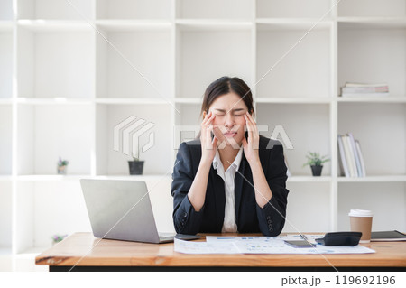 Stressed Business Woman Working at Desk with Laptop and Documents in Modern Office Environment Stressed Business Woman Working at Desk with Laptop and Documents in Modern Office Environment 119692196