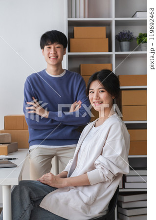 Young Couple Running a Small Online Business from Home, Surrounded by Shipping Boxes and Office Supplies, Smiling and Confident in Their Modern Workspace Young Couple Running a Small Online Business from Home, Surrounded by Shipping Boxes and Office Supplies, Smiling and Confident in Their Modern Workspace 119692468