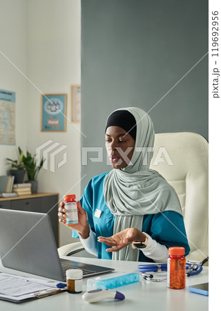 Muslim Woman Sitting in an Office Holding Pills 119692956