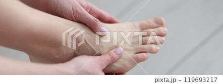 Woman massages painful foot joints with hands in light room Woman massages painful foot joints with hands in light room 119693217