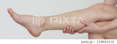 Woman massages shin muscles sitting on white background Woman massages shin muscles sitting on white background 119693218
